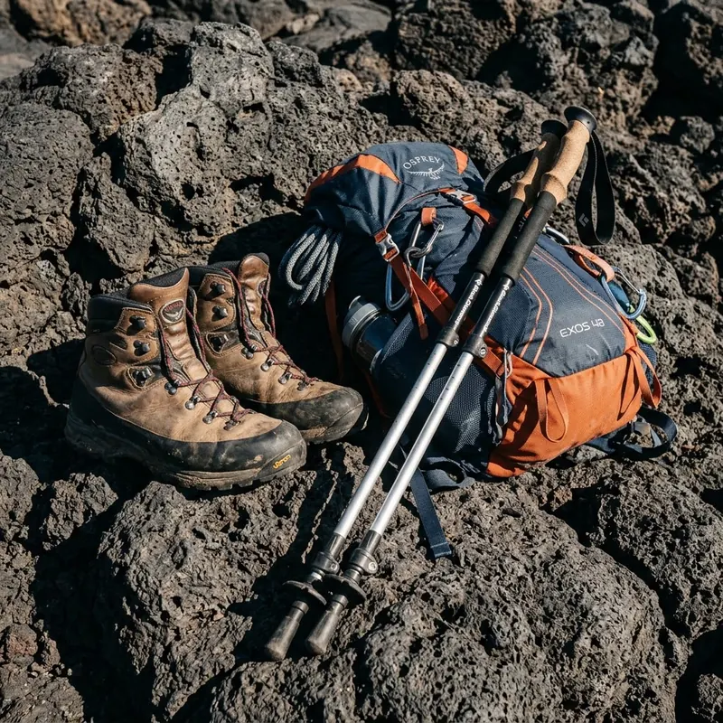 Botas de montaña, bastones y mochila técnica sobre roca volcánica oscura