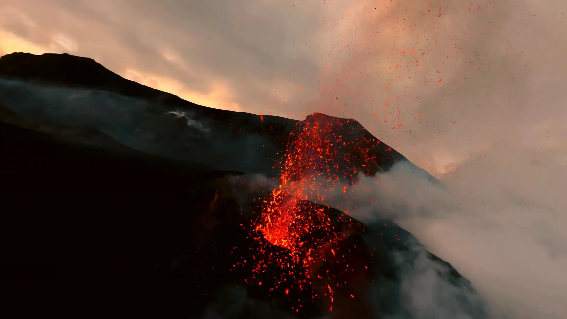 Vuelo de dron sobre un cráter en erupción que lanza lava al atardecer